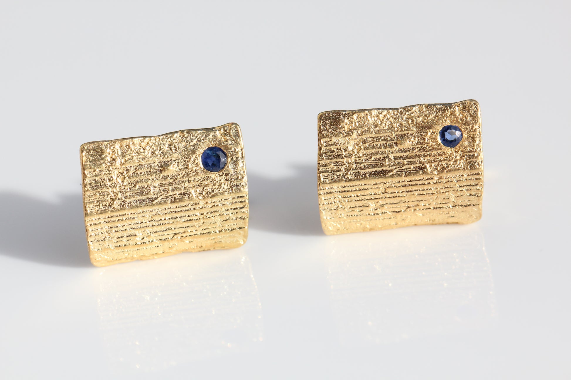 Picture of gold cufflinks for men with blue sapphires set in the bark texture.