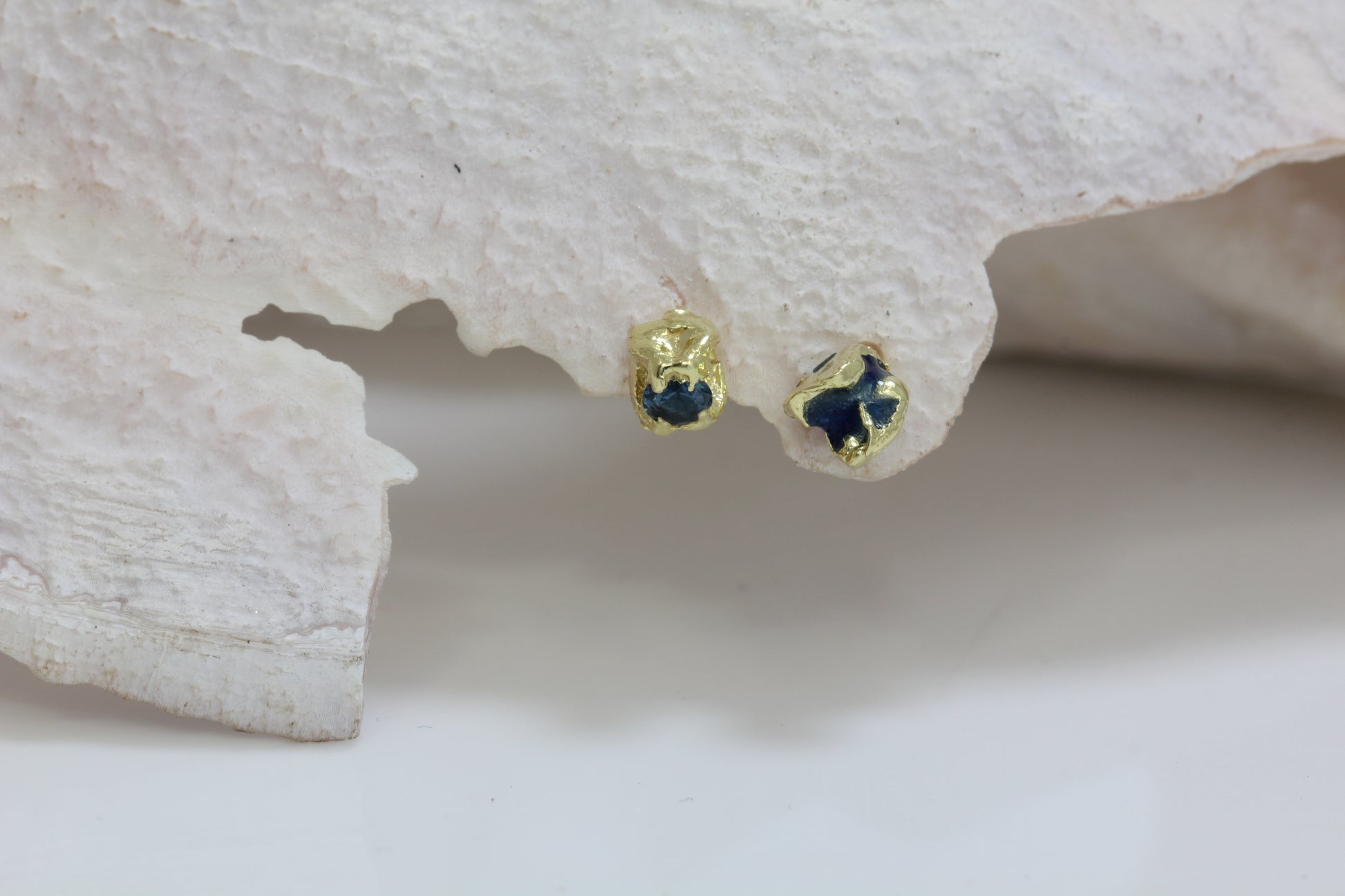 Showing on a shell 18 carat yellow mis matched earring studs with blue enamel and blue sapphire.