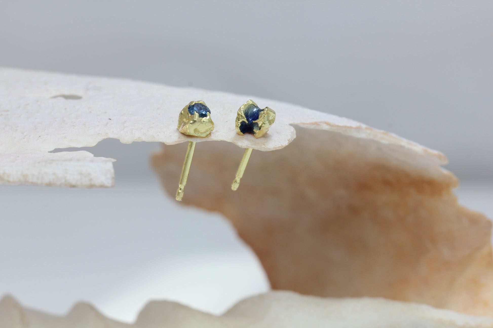 Showing on a shell and stud back 18 carat yellow mis matched earring studs with blue enamel and blue sapphire.