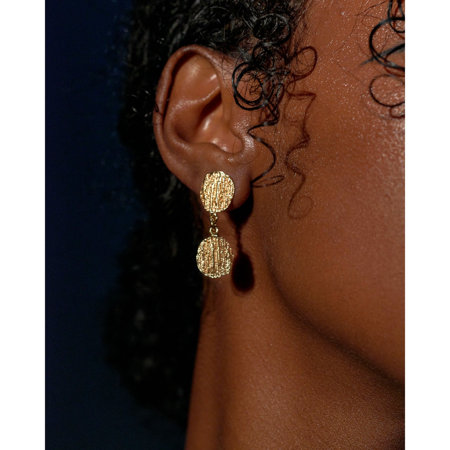 Picture of a model wearing gold bark textured drops earrings which look very sophisticated being worn.