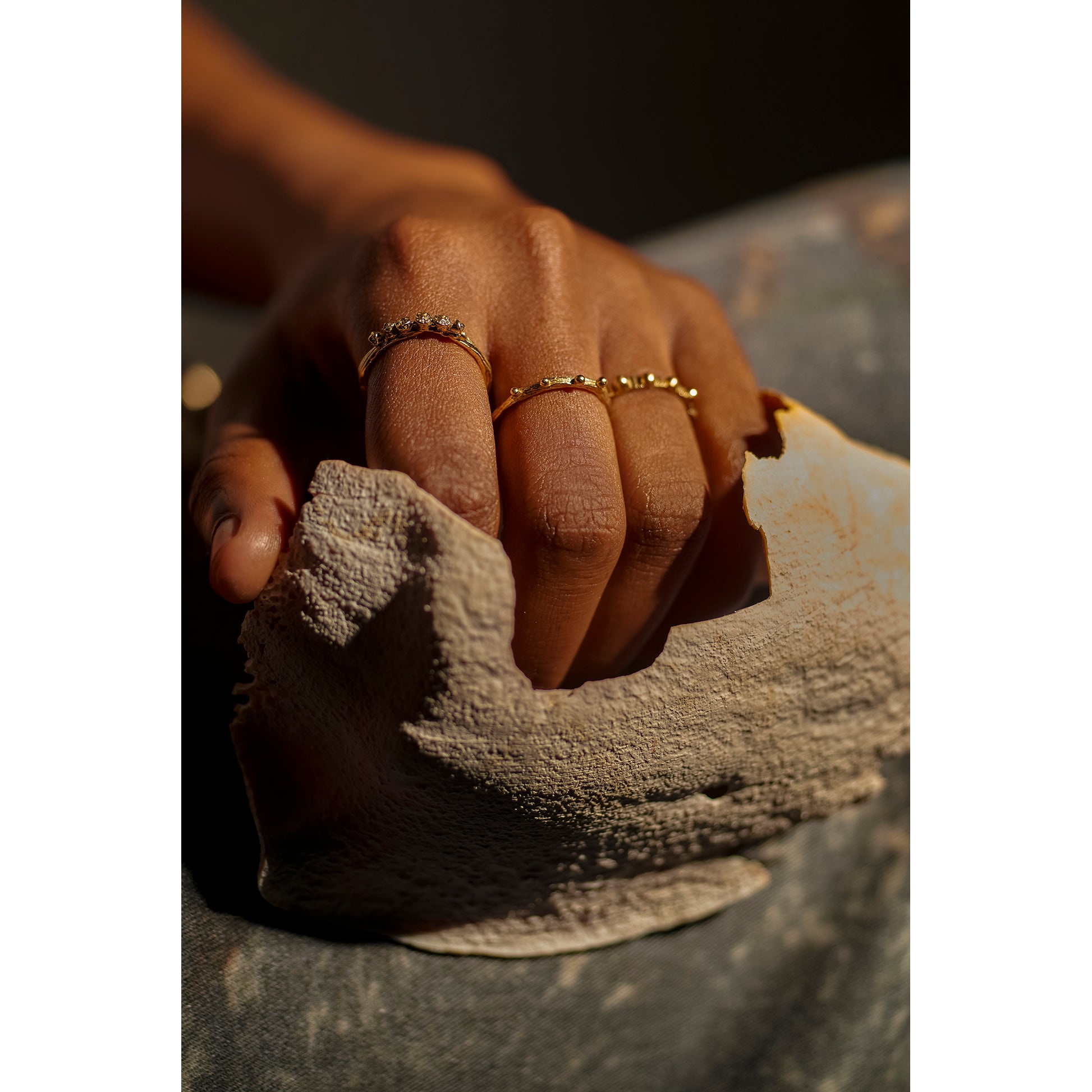 Models hand wearing three textured rings cast from twigs in gold.