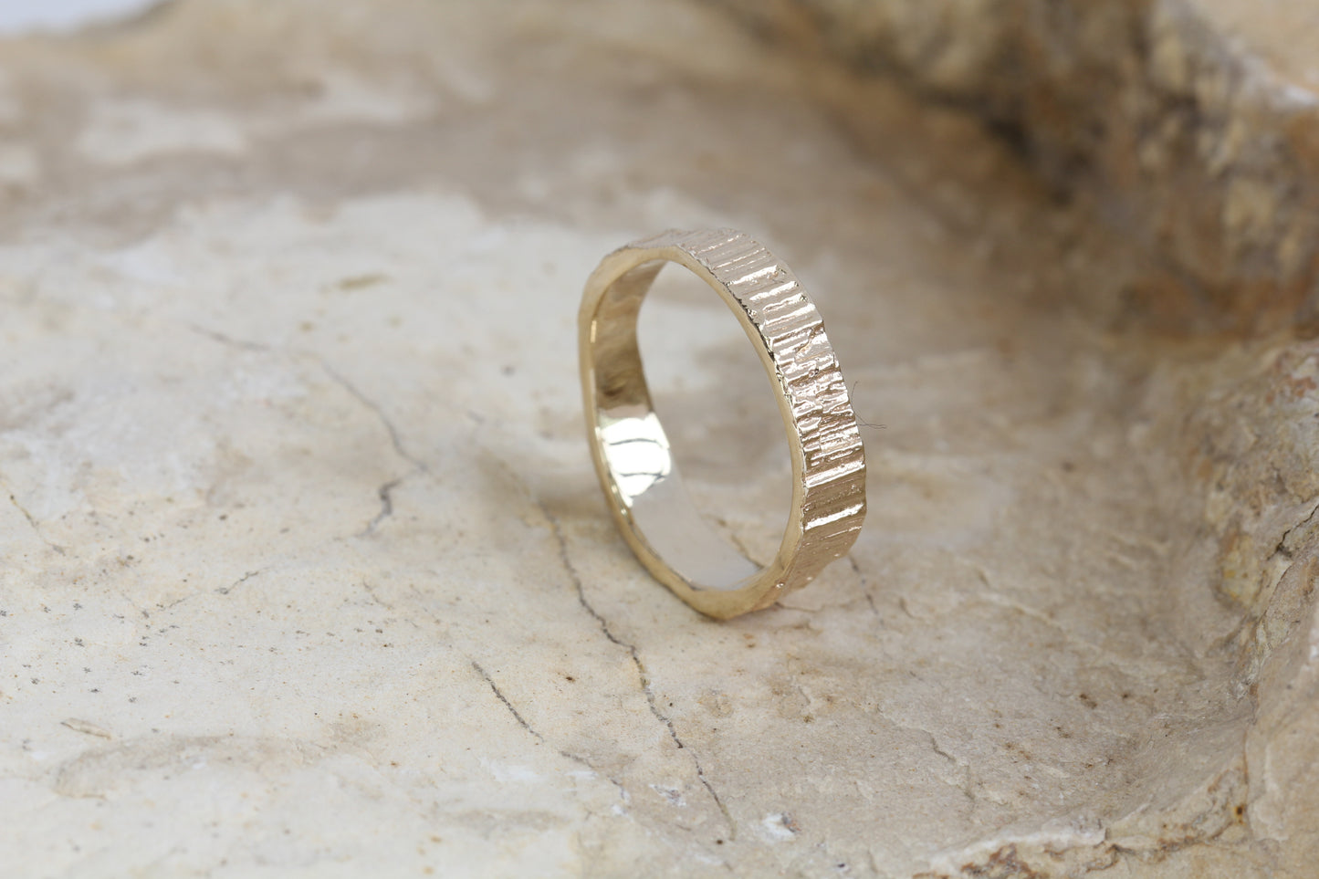 A gold ring standing on a rock. Alternative wedding band with organic textures and smooth polished inside.. Handmade by Irish jeweller Eily O Connell.