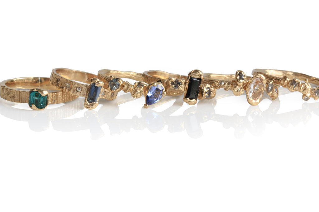 gold rings lying in a row with sapphires, black diamonds and rough diamonds