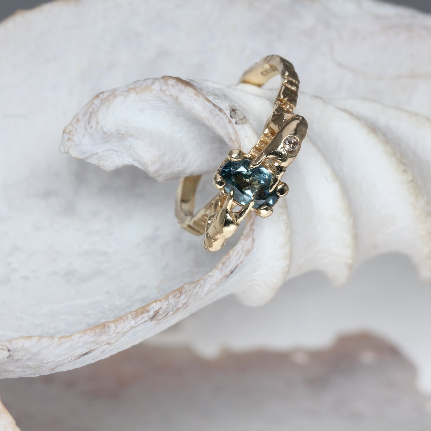 Alternative gold engagement ring with blue sapphire and champagne diamond with crab claws holding the blue precious gemstone. 
