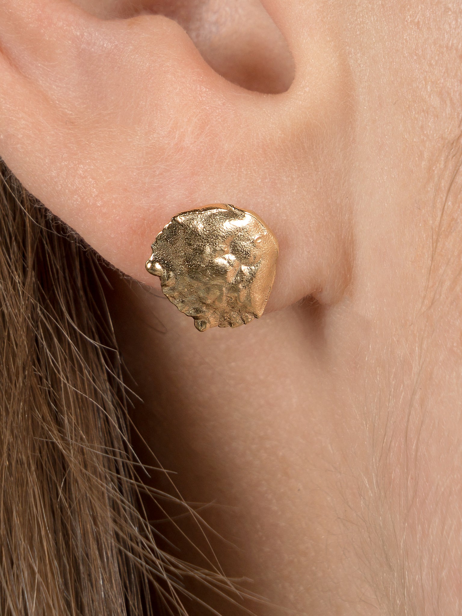 Gold crab shell stud being worn on an ear. Close up shot of a single earring cast from crab shell.