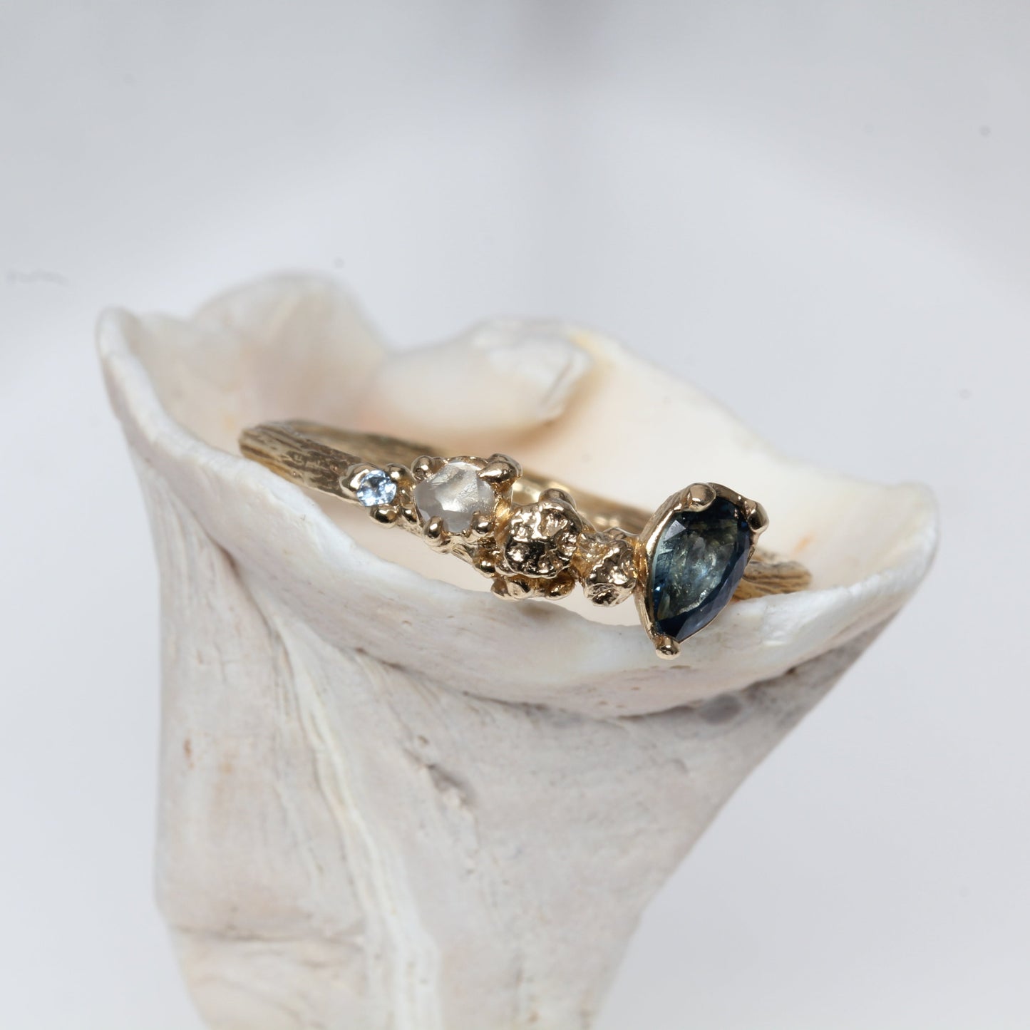 Gold ring with a blue sapphire gemstone on a white shell against a light gray background