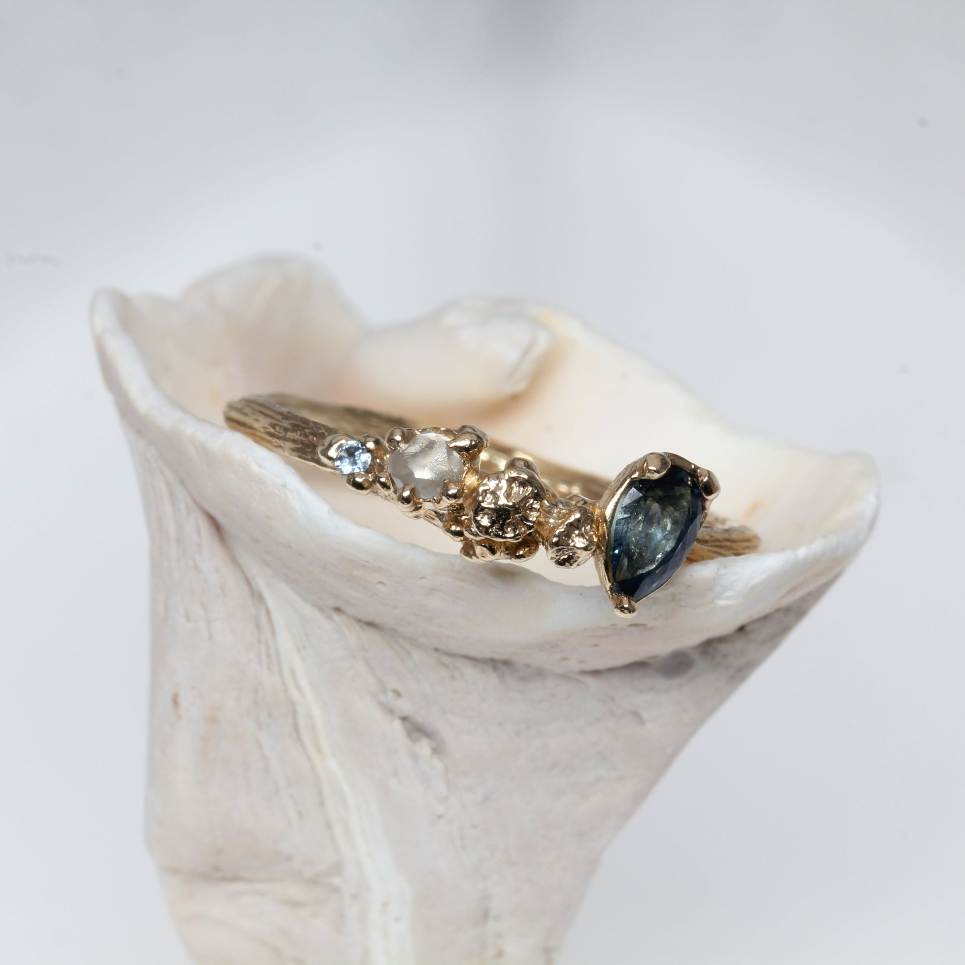 Gold ring with a blue sapphire gemstone on a white shell against a light gray background