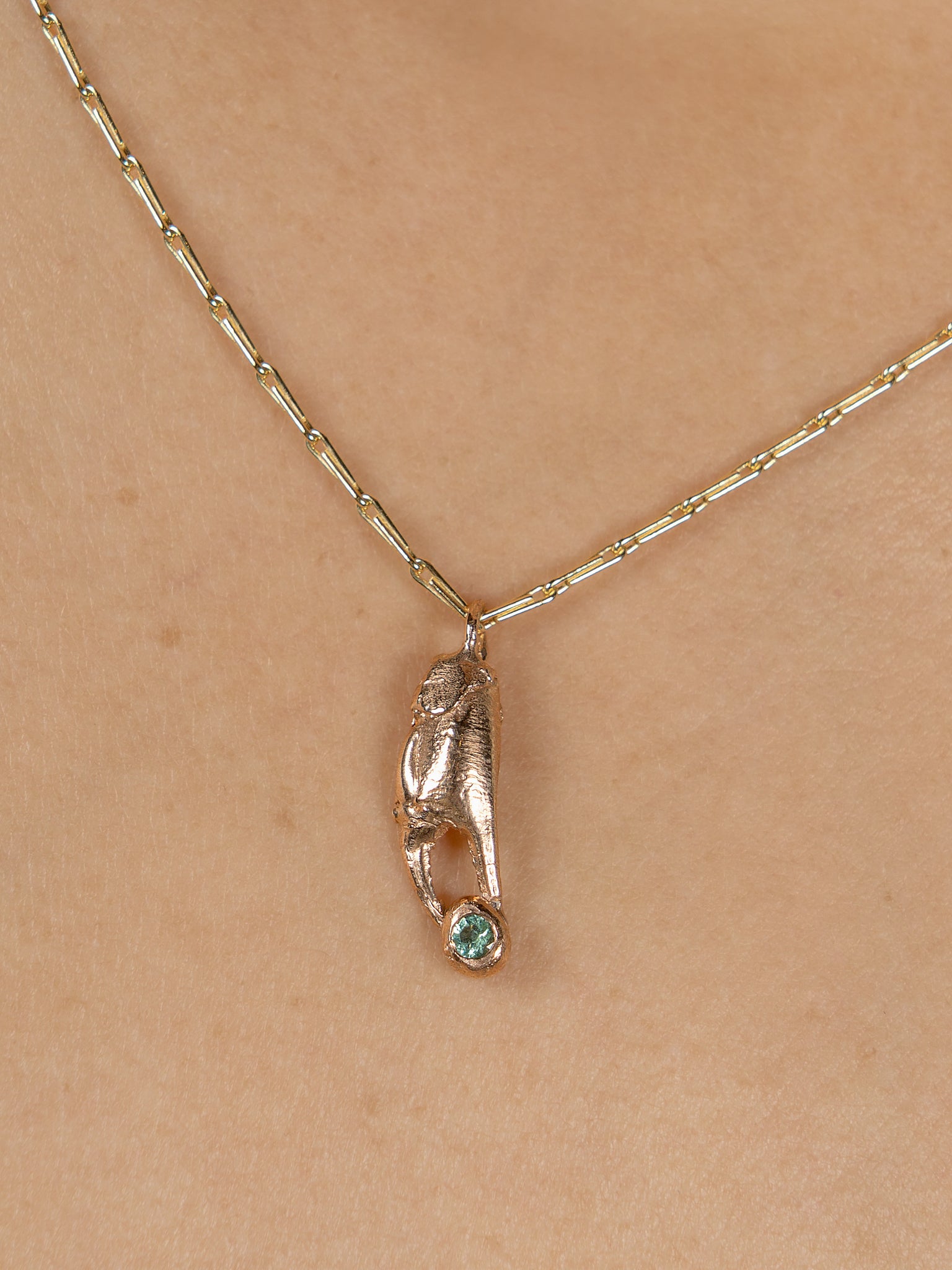 Red gold crab claw on a yellow gold chain holding green tourmaline gemstone which is Fairtrade.  Shown close up on skin.
