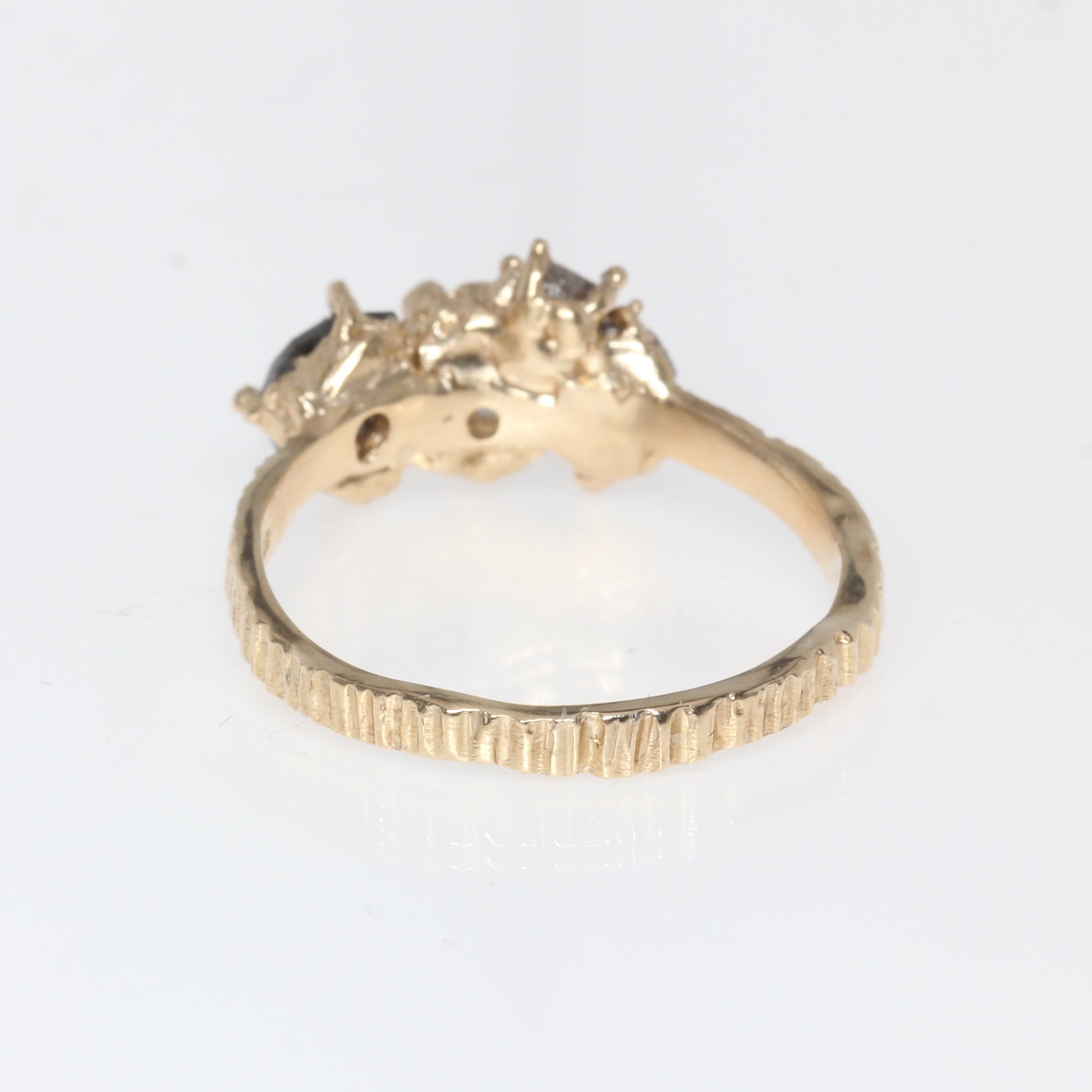 A gold ring with a textured band and a cluster of small clear stones at the top, photographed on a plain white background.