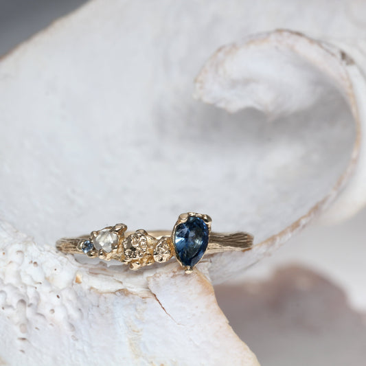 Gold engagement ring with a blue sapphire, raw white diamond  on a white shell