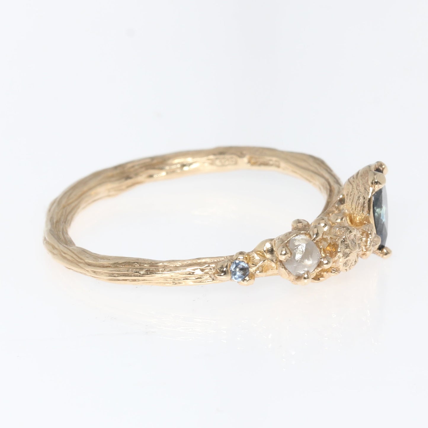 Gold ring with a off centre sapphire gemstone and raw diamond on a white background