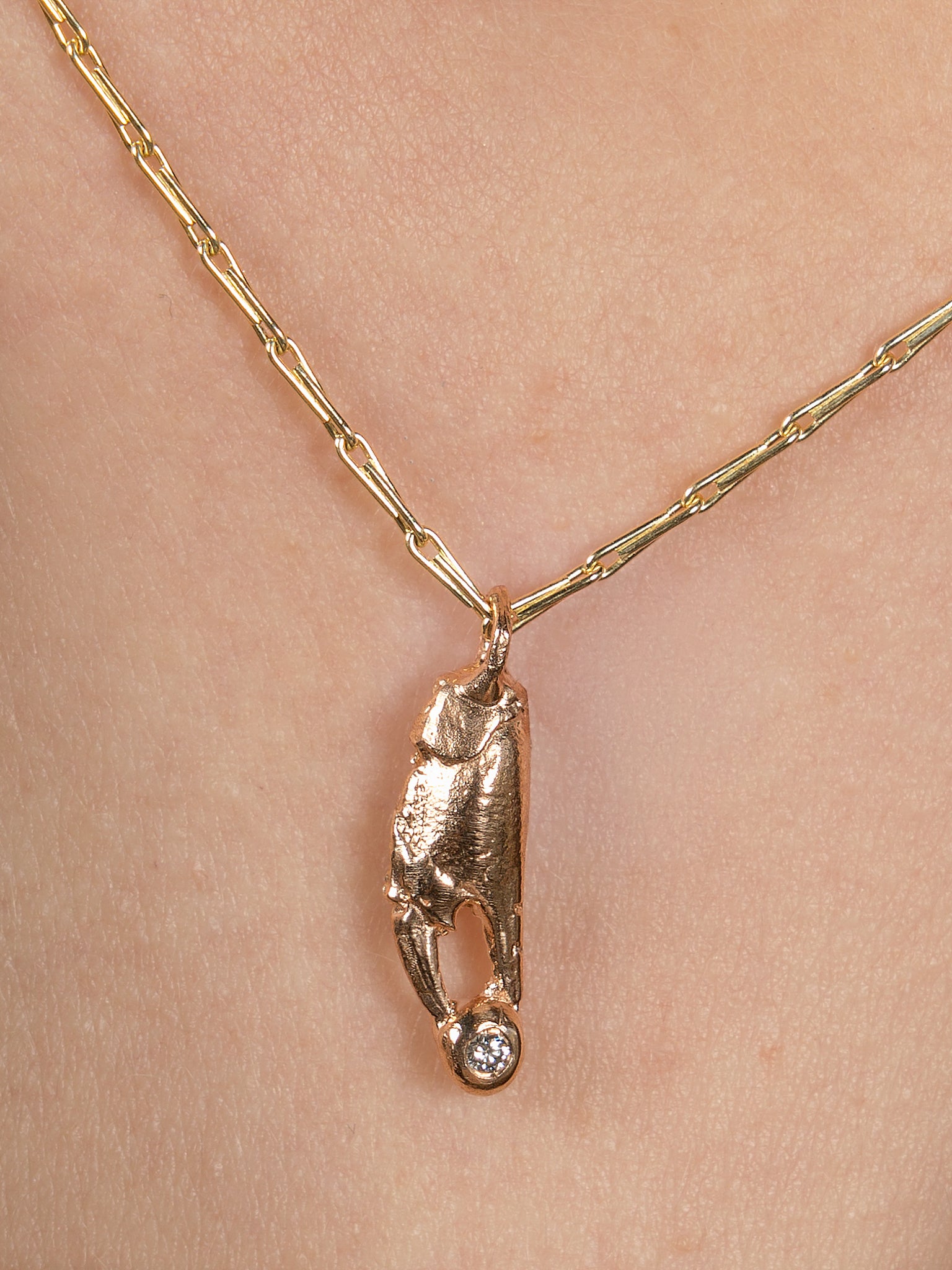 Red gold crab claw on a yellow gold chain holding a diamond close up picture with skin. 
