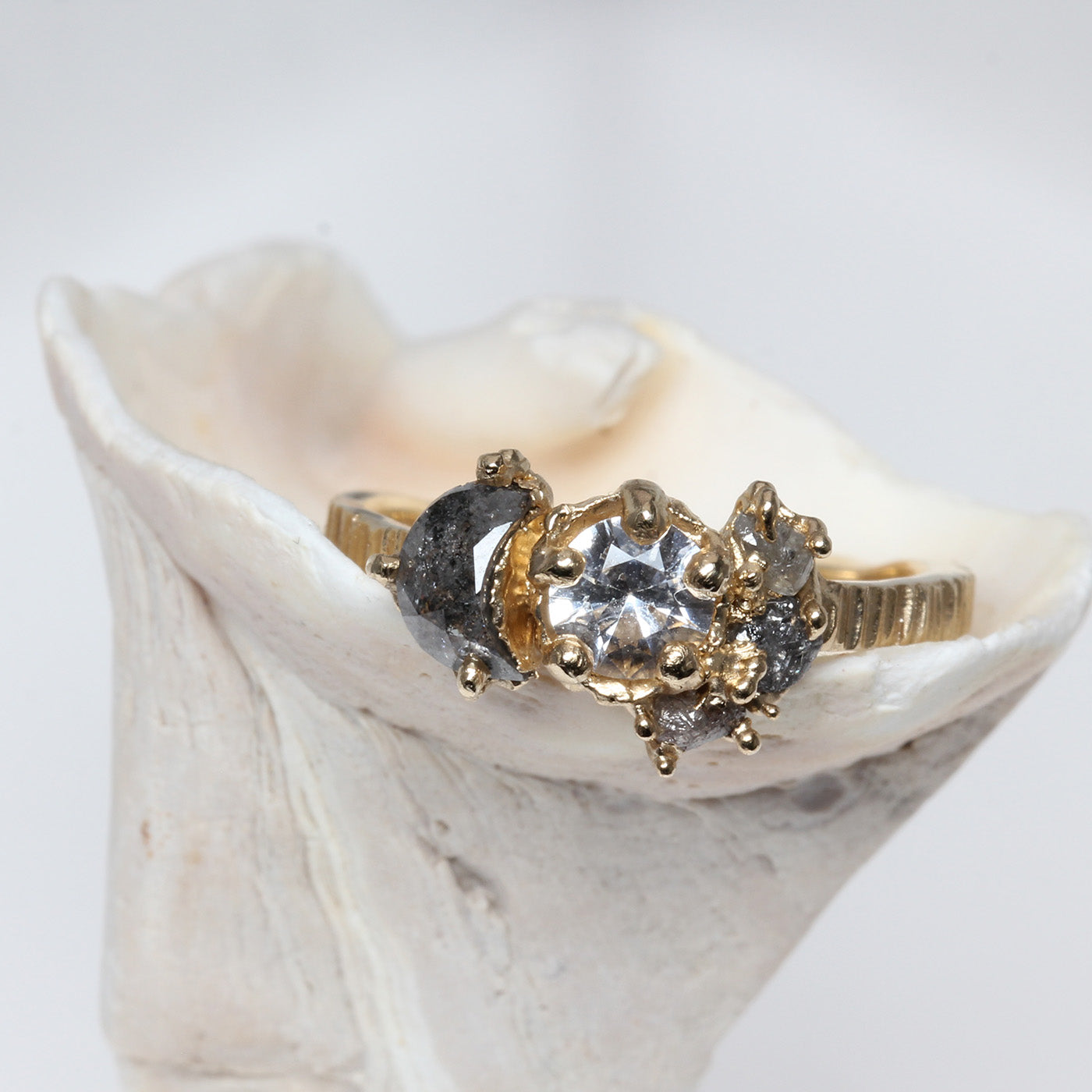 Gold ring with a central white sapphire gemstone and smaller diamonds on a white shell background. Inspired by the sun, stars and moon
