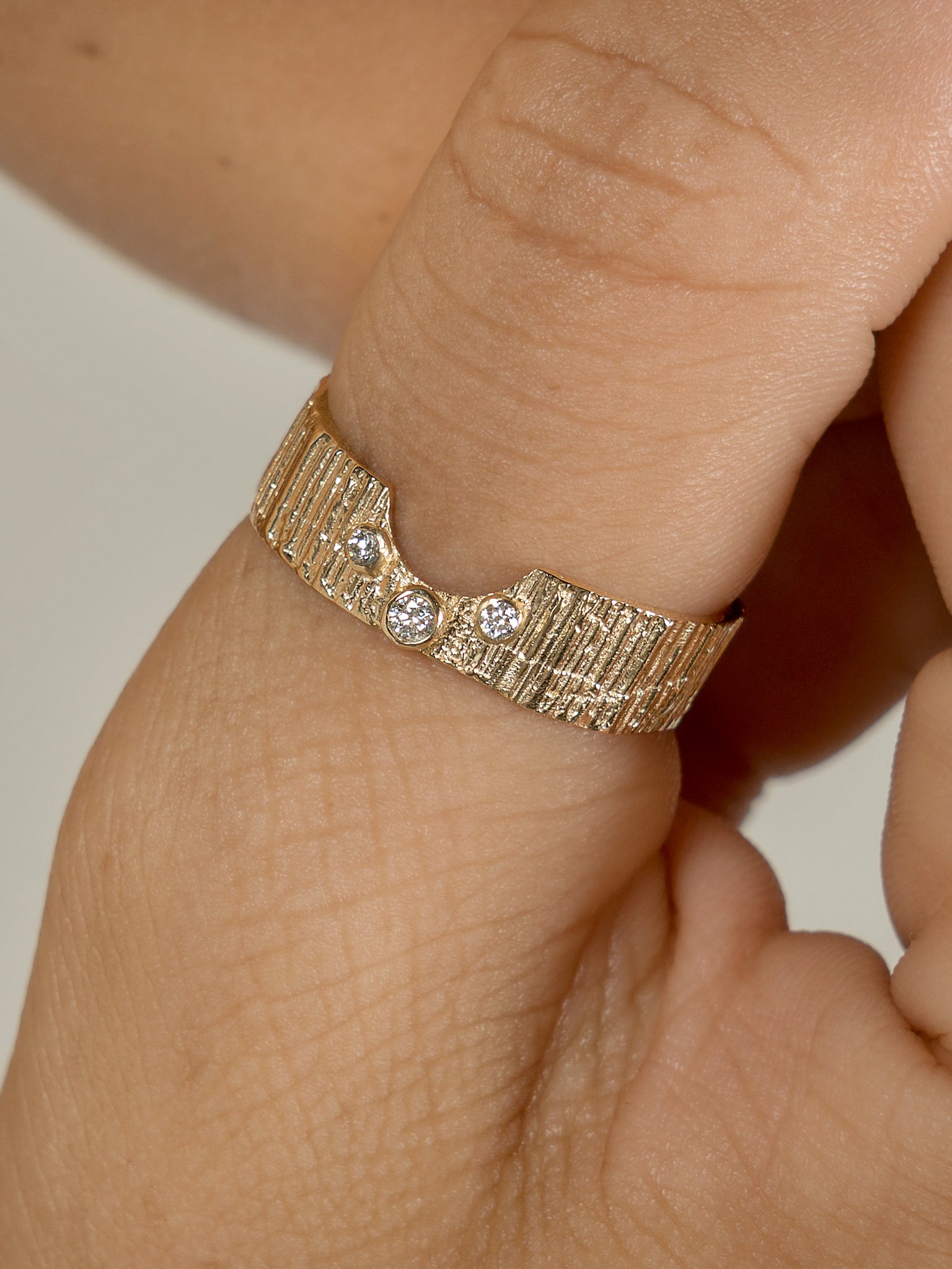 Picture of a textured wedding band with three diamonds set in middle. U shape groove in ring to fit with other rings. Close up image if ring on a finger. 