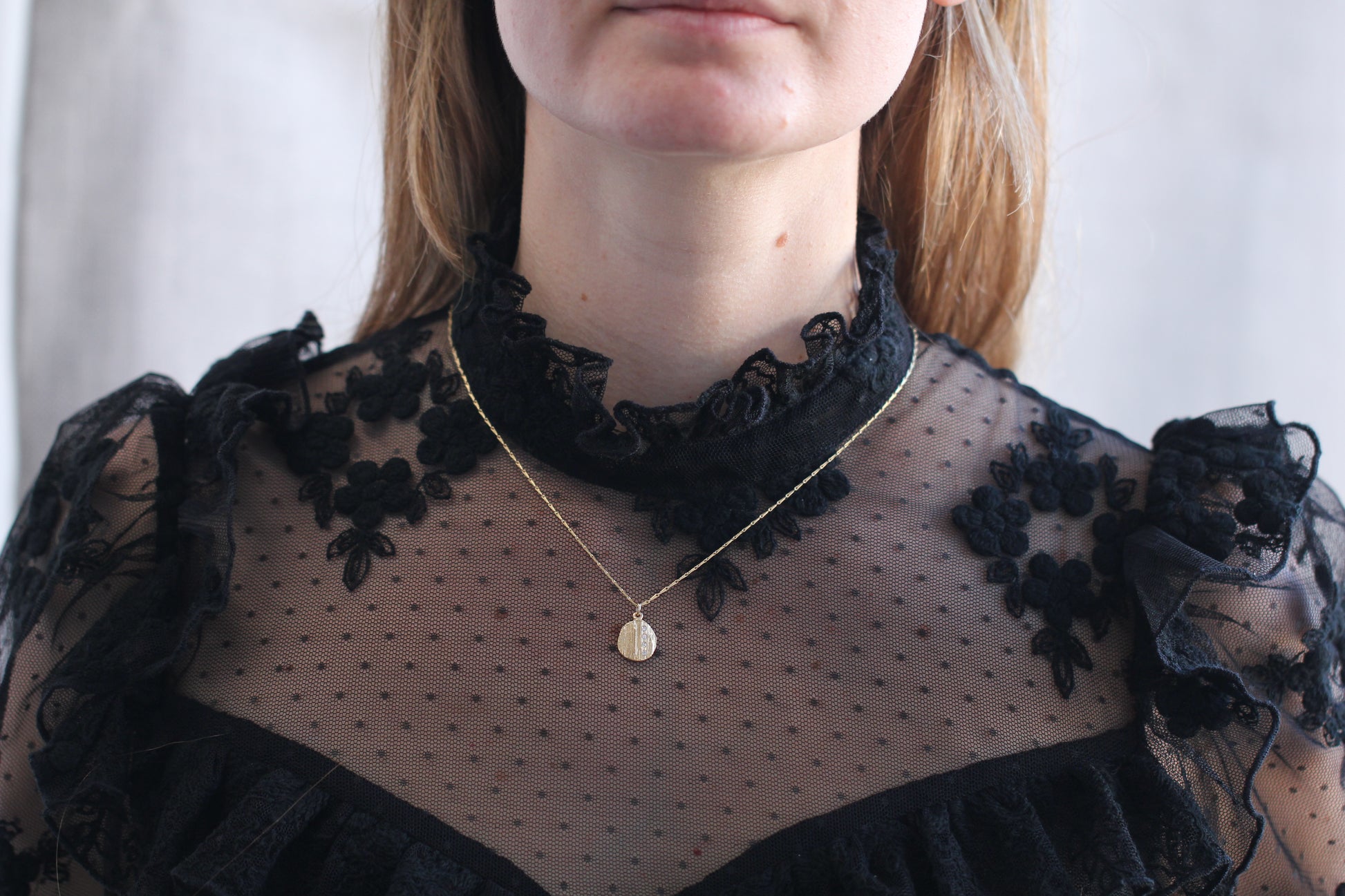 Person wearing a black lace top with a gold necklace against a white background