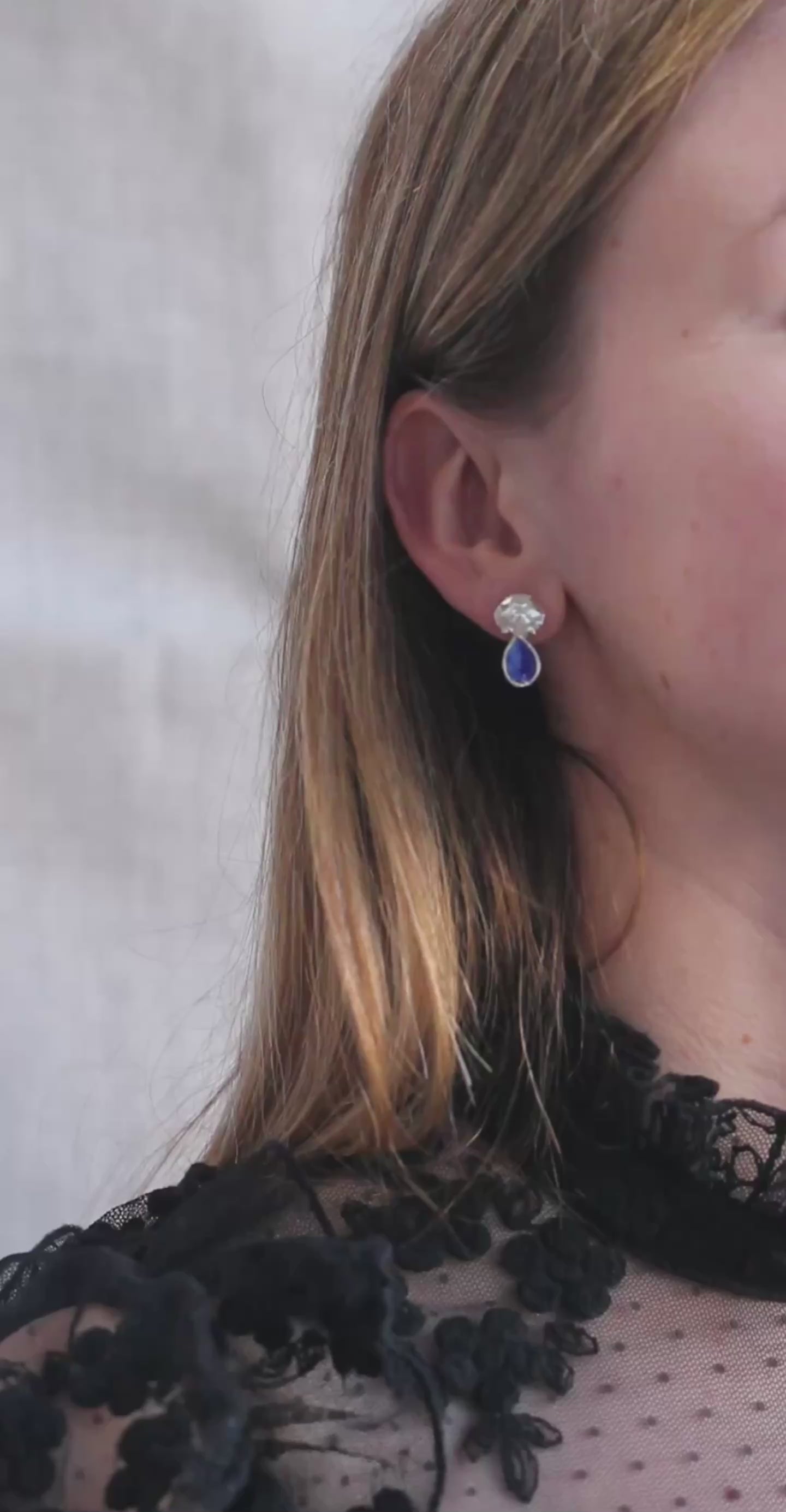 Silver earrings in the shape of crab shells with blue enamel drop that looks like a blue sapphire gemstone shown here on a model. 