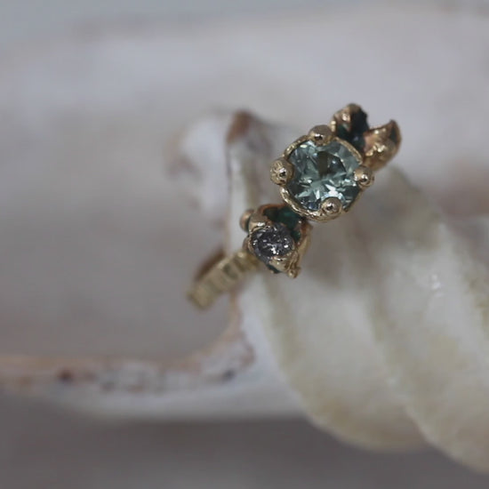 Alternative engagement ring handmade in gold and cast from nature. IThis ring features a green sapphire, green enamel and a salt and pepper diamond. Handmade by irish jeweller eily o connell in Bristol. You can hear sounds of the sea in the background to video and the ring is on a shell.