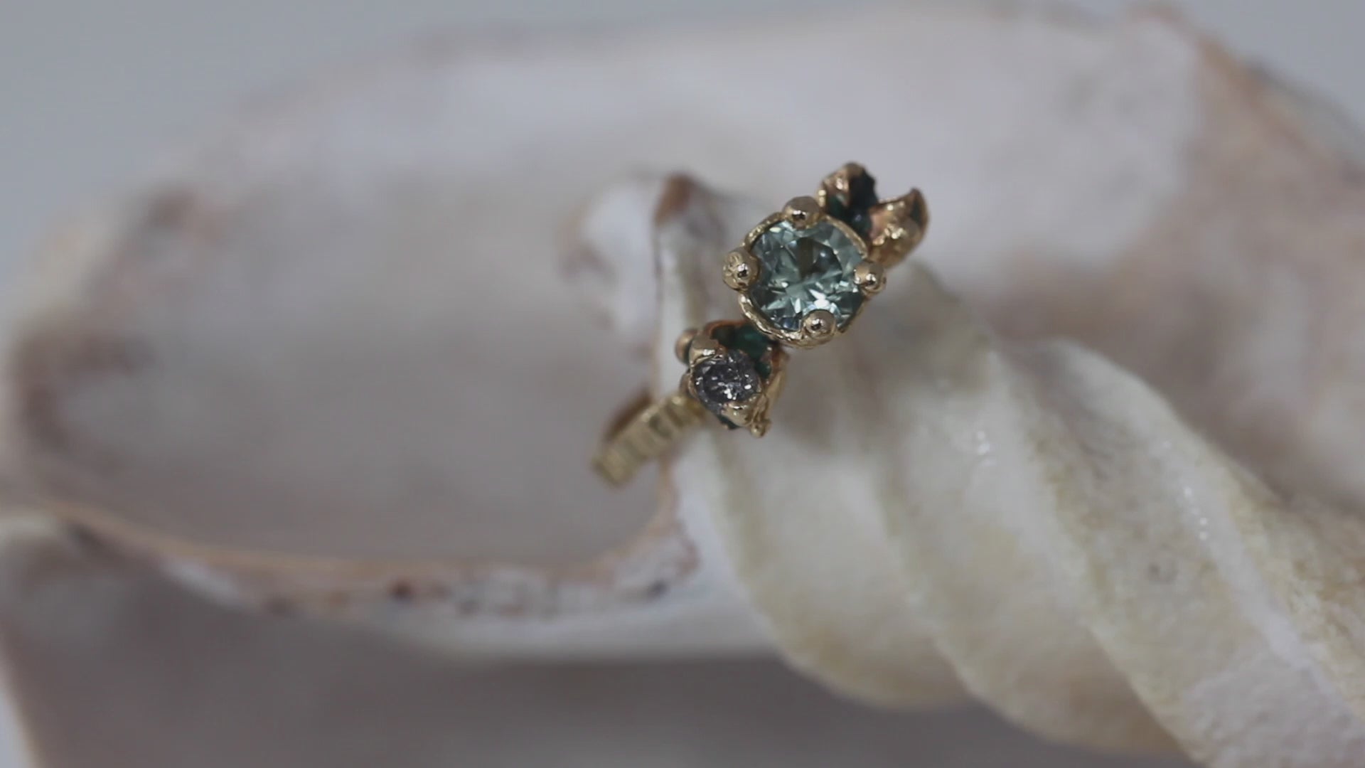 Alternative engagement ring handmade in gold and cast from nature. IThis ring features a green sapphire, green enamel and a salt and pepper diamond. Handmade by irish jeweller eily o connell in Bristol. You can hear sounds of the sea in the background to video and the ring is on a shell.
