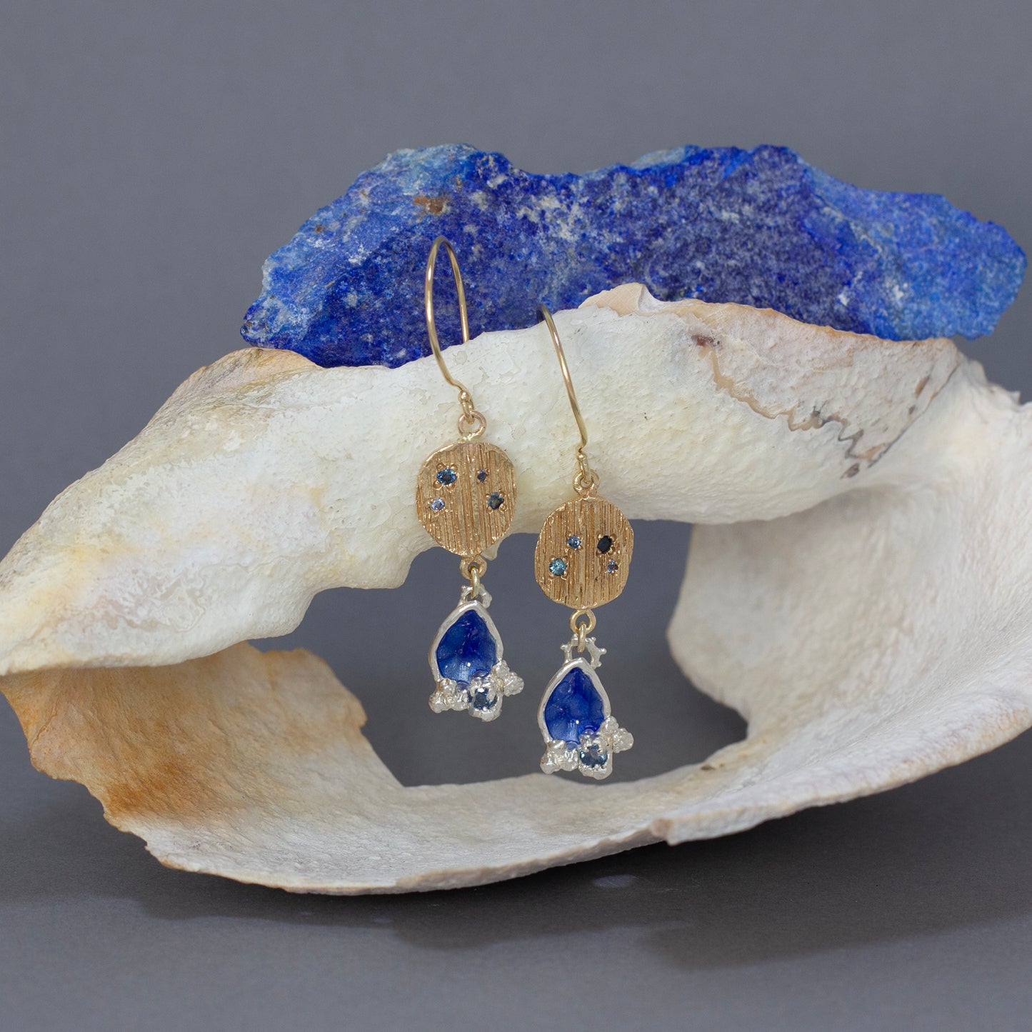 Handmade gold and sapphire earrings with enamel and a lapis lazupli in azure blue in background.