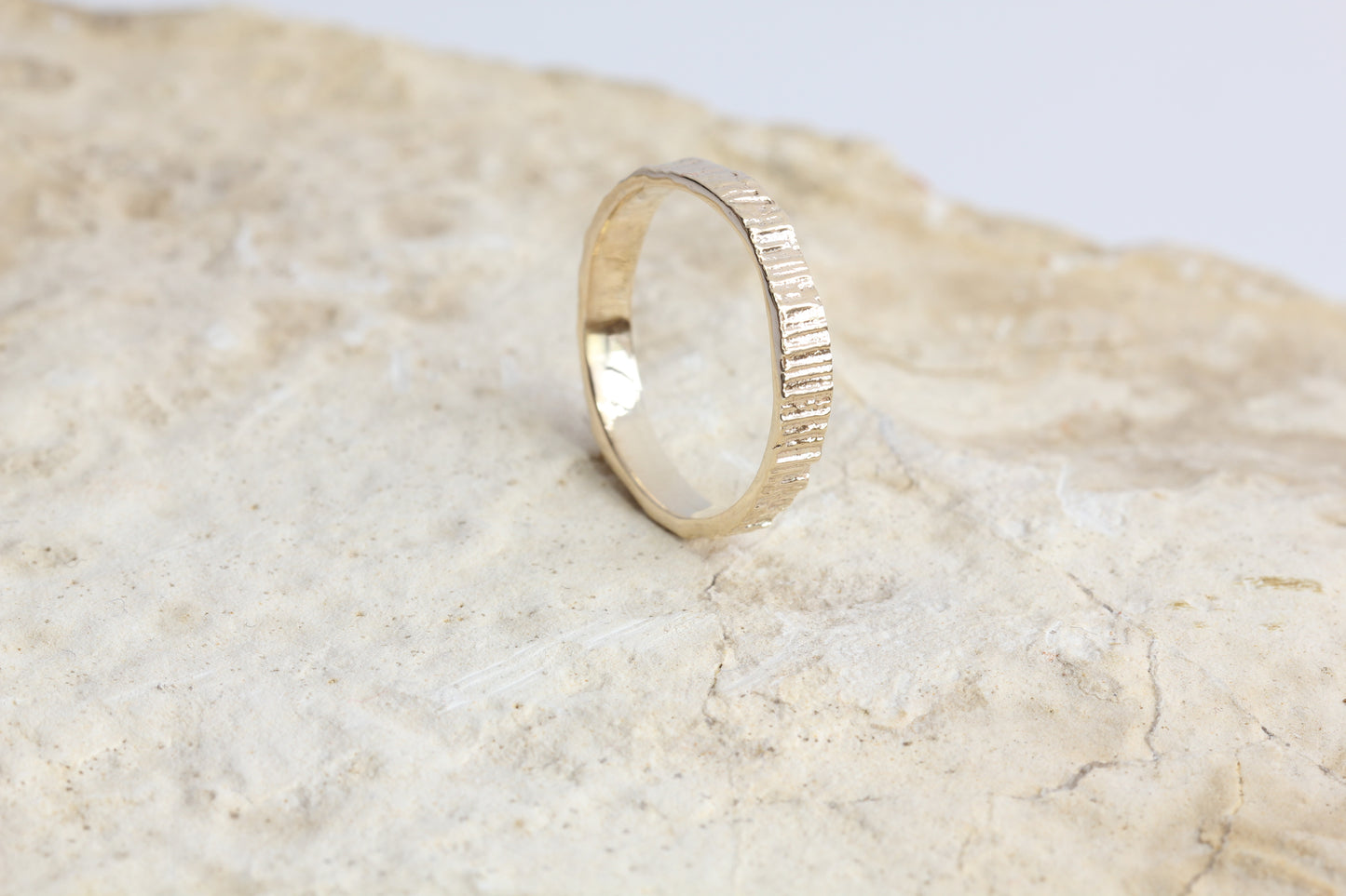Tree textured gold wedding band shown on a rock.