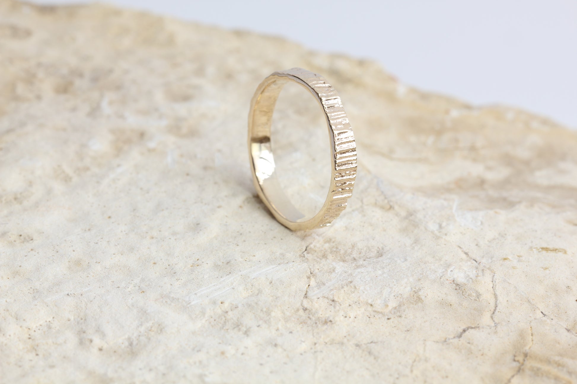 Tree textured gold wedding band shown on a rock.