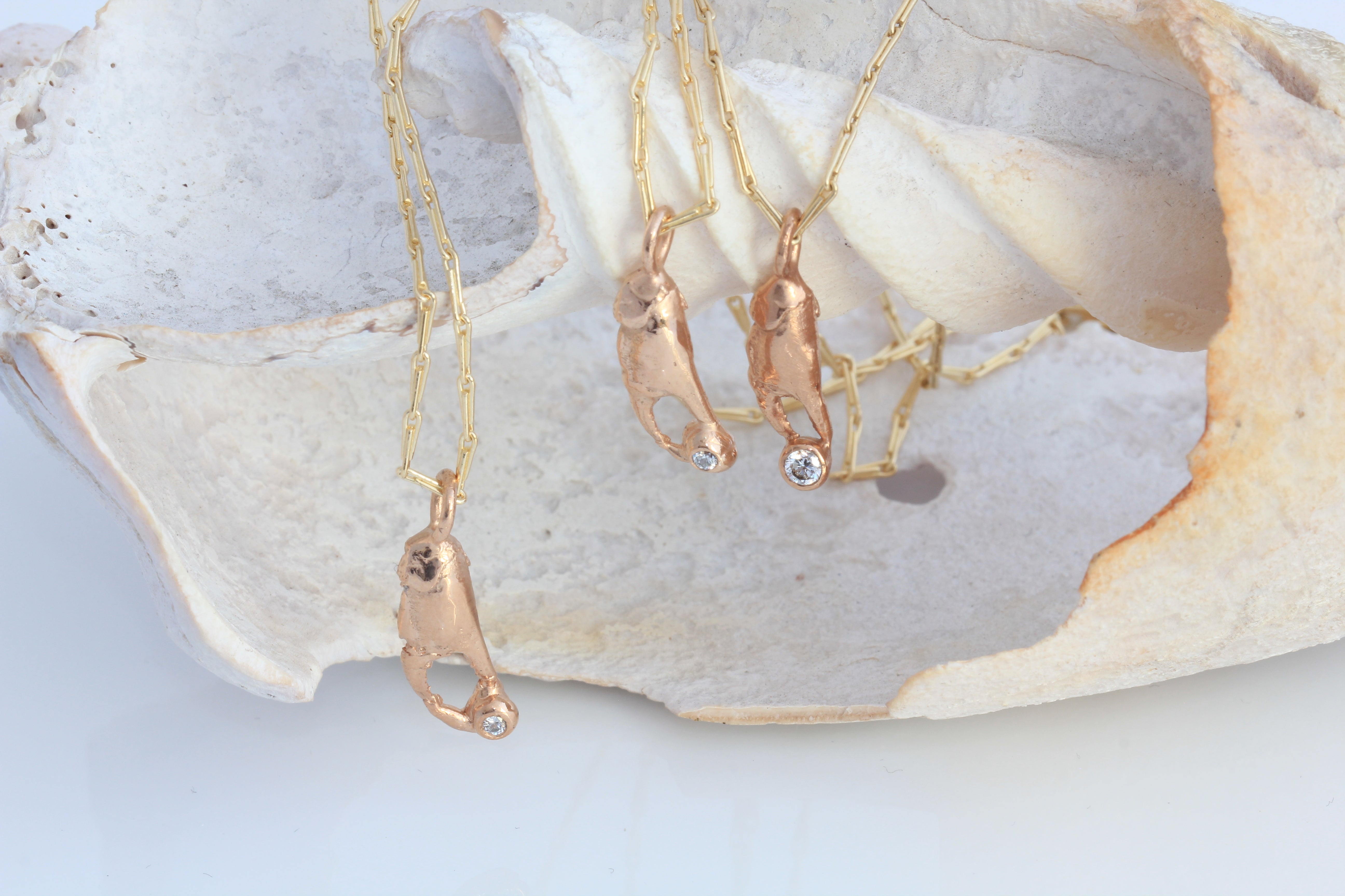 Three yellow gold chains with crab claw pendants in red gold holding diamonds. Each pendant is cast from a tiny crab claws and they are photographed here on a shell. .  