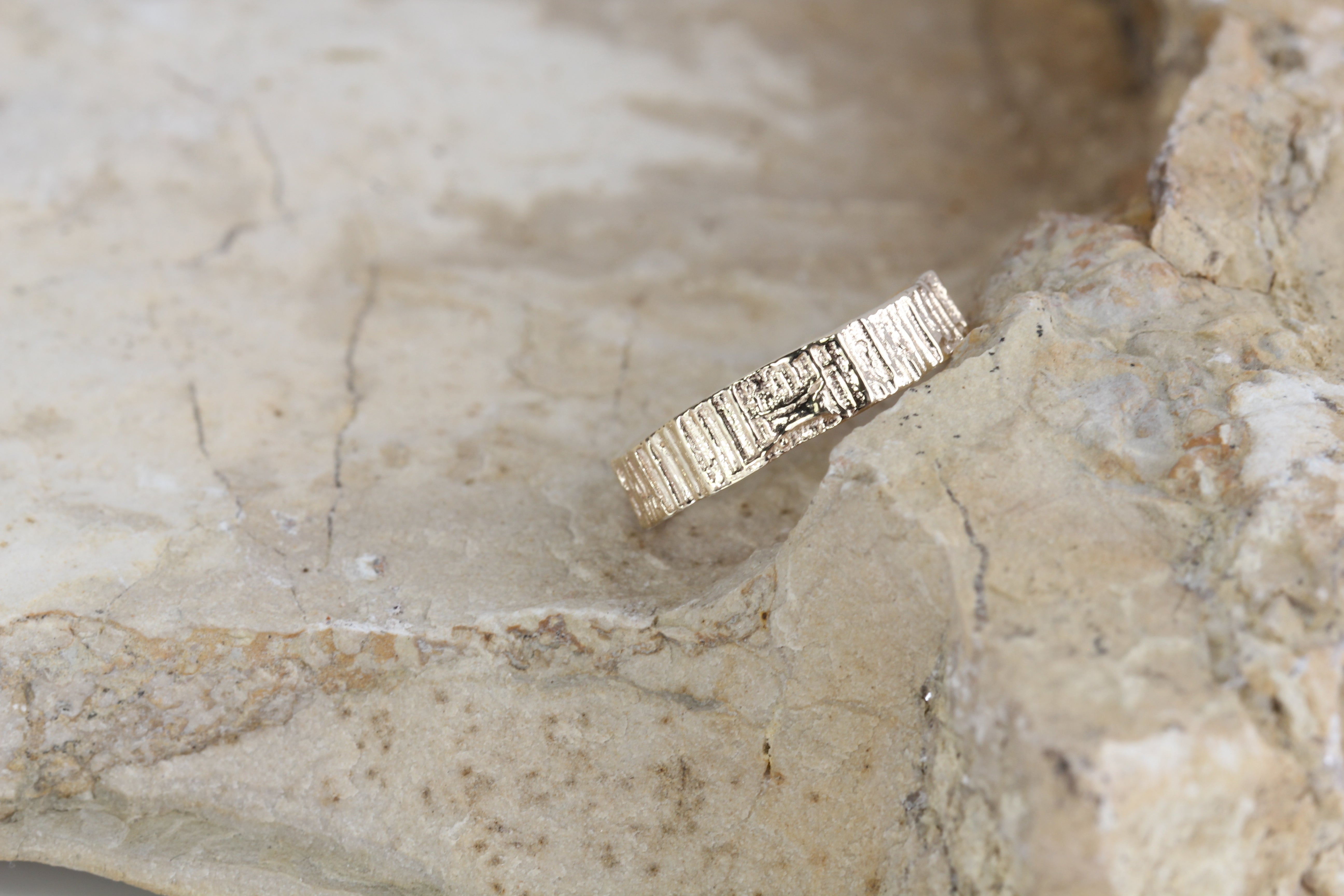 Alternative wedding band or gold ring with organic textures. Close up picture of grooves sitting on a rock. Handmade by Irish jeweller Eily O Connell.