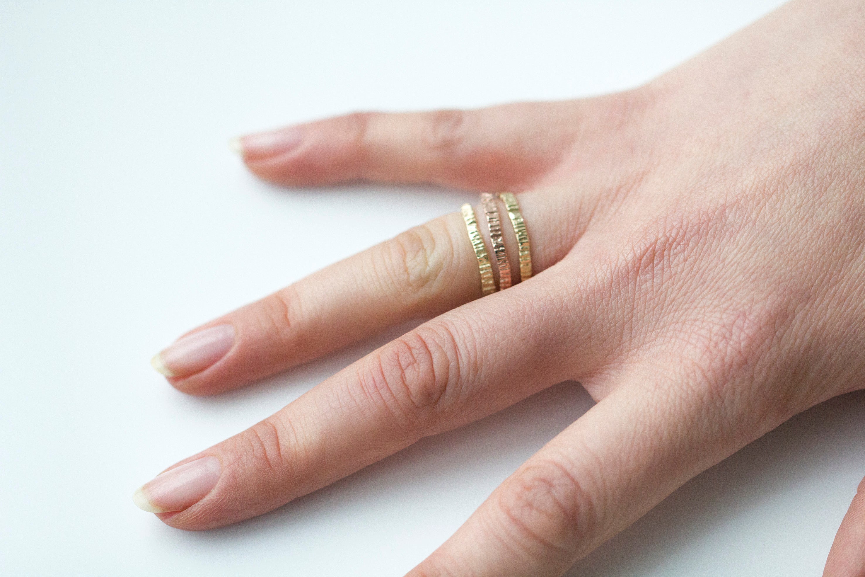 Picture of a hand with gold alternative wedding bands. These rings are stacked on one finger. They have been cast from bark so it has organic grooves and textures. Handmade by Irish jeweller Eily O Connell who lives in Bristol. 